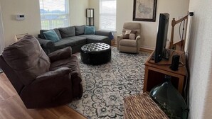 A living room with a sectional sofa, a single armchair, a coffee table, a television, and a ceiling fan. - Budget friendly, fun, great location & clean! You found your next vacation home. (Surfside Beach)
