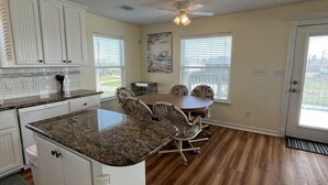 A kitchen with white cabinets, a granite countertop, and a dining area with a table and chairs. - Budget friendly, fun, great location & clean! You found your next vacation home. (Surfside Beach)