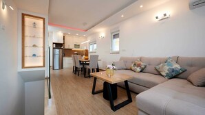 A modern living room with a sofa, a dining table with chairs, and a kitchen in the background.