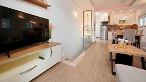 A modern kitchen with a large TV, wooden shelves, and a dining area with a table and chairs.