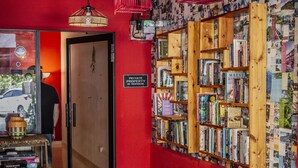 A room with a red wall, a bookshelf filled with books, a wooden shelf, and a door. - House of Lion Hostel and Guesthouse (Langkawi)