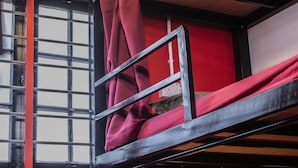A bunk bed with red bedding, a window with bars, and a wall-mounted light fixture. - House of Lion Hostel and Guesthouse (Langkawi)