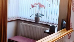 A room with a large mirror, a window with vertical blinds, a radiator, and a small bench. - Immaculate 3-bed House in Durham Near Sedgefield (Trimdon Station)