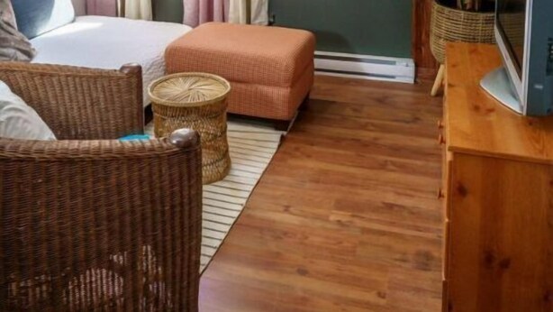 Een gezellige slaapkamer met een bed, een houten vloer, een rieten stoel, een klein tafeltje en een televisie op een houten dressoir.