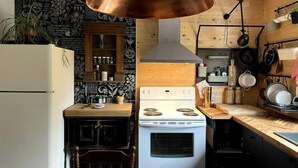 Een compacte keuken met een witte kookplaat, een houten aanrechtblad en een hangende koperen lamp.