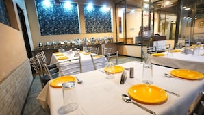 A restaurant with multiple tables set for dining, each with yellow plates, cutlery, and clear glasses. - Igatpuri Hill Retreat (Igatpuri)