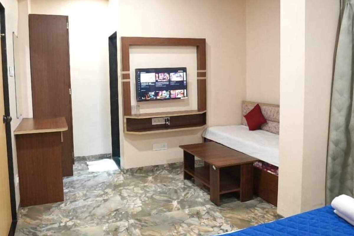 A hotel room with a bed, a TV mounted on the wall, a small desk, and a wardrobe.
