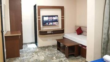 A hotel room with a bed, a TV mounted on the wall, a small desk, and a wardrobe.