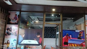A room with a large window, a ceiling fan, and a poster of a child playing table tennis. - Igatpuri Hill Retreat (Igatpuri)