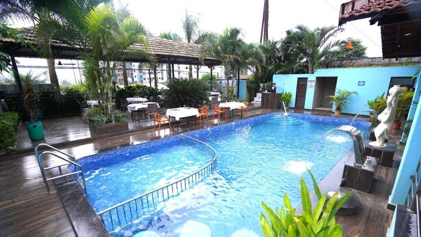 An indoor swimming pool with a tiled edge, surrounded by tables and chairs, and various plants. - Igatpuri Hill Retreat (Igatpuri)