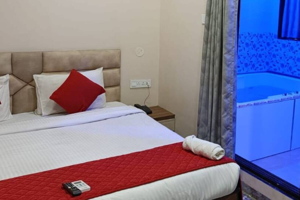 A hotel room with a bed, a red quilt, a white pillow, and a red pillow.