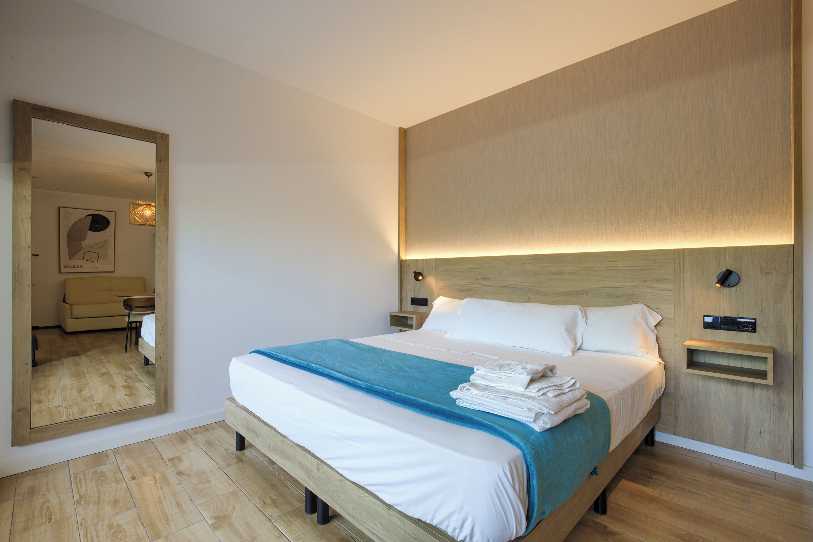 Una cama bien hecha con una colcha azul, un cabecero de madera y una mesita de noche con una lámpara.