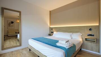 Una cama bien hecha con una colcha azul, un cabecero de madera y una mesita de noche con una lámpara.