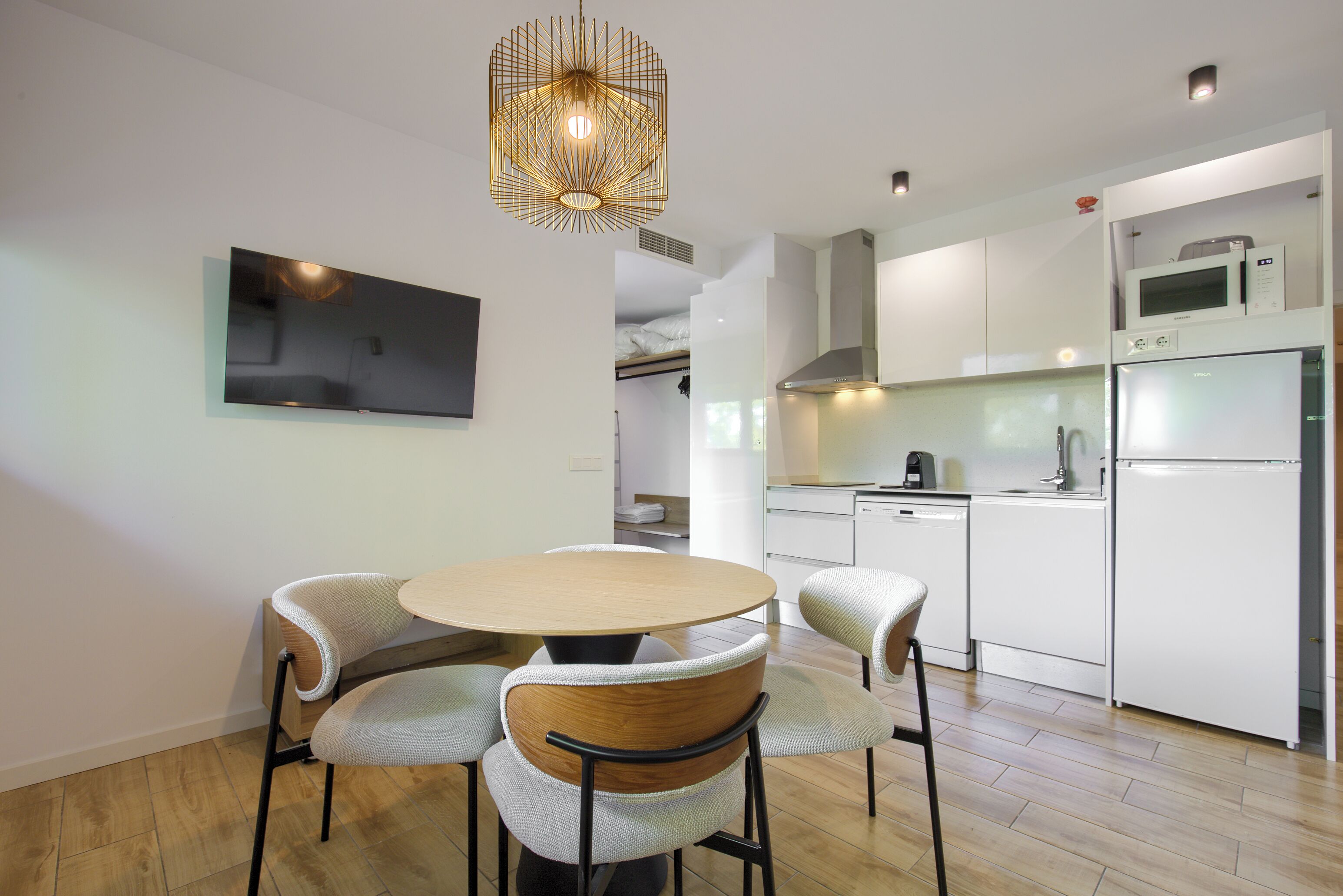 A modern kitchen with white cabinets, a microwave, a refrigerator, and a dining area with a round table and four chairs.