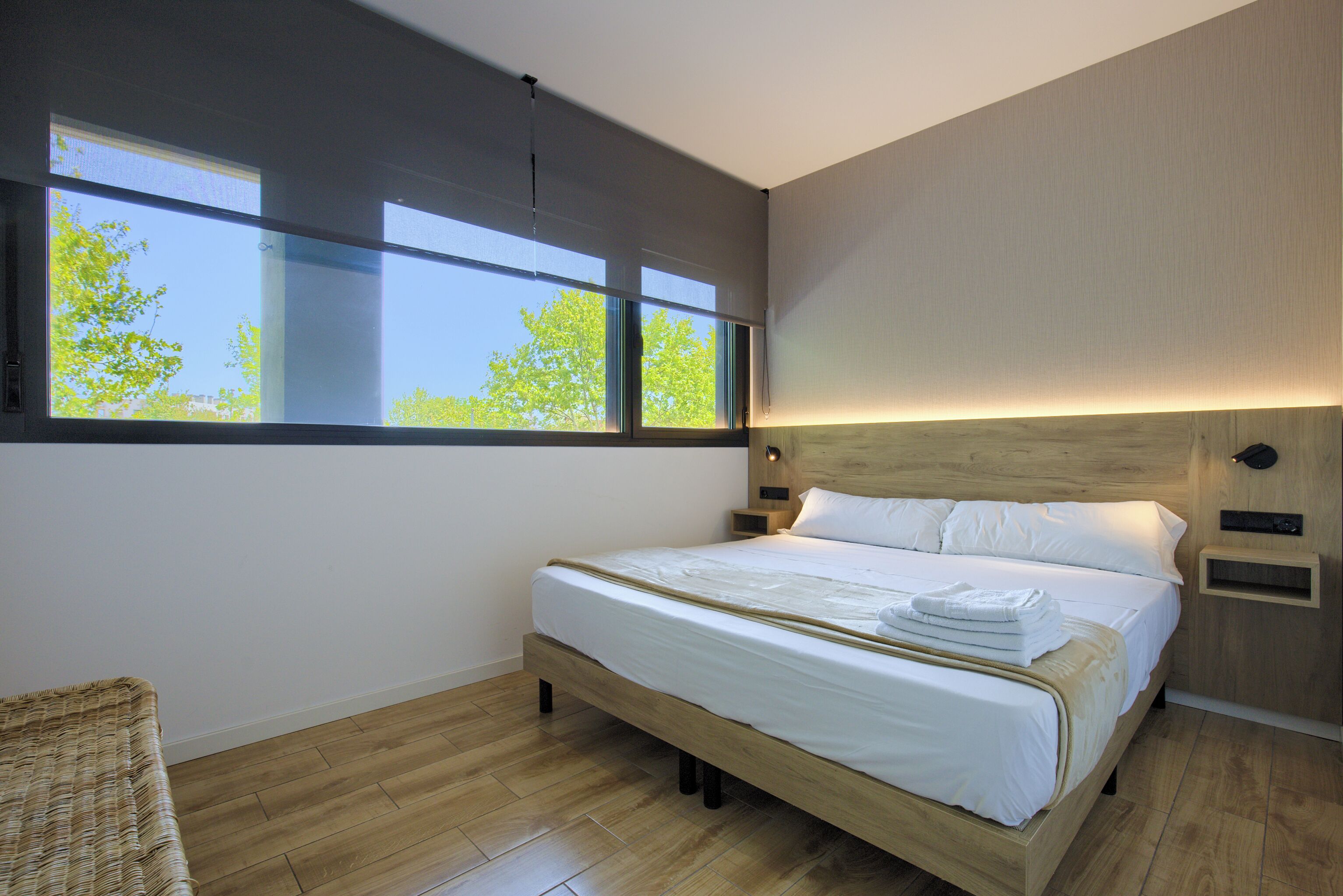 Un dormitorio moderno con una cama grande, suelo de madera y vistas a árboles por las ventanas.