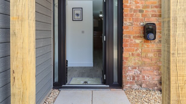 A wooden door with a glass panel, a welcome mat, and a small framed picture on the wall. - Bumblebee Cottage (Wellington)