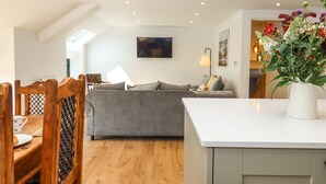 A modern living room with a grey sofa, wooden dining chairs, a white coffee table, and a vase of flowers. - Bumblebee Cottage (Wellington)