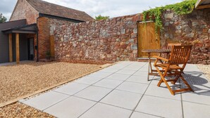 A patio area with a stone wall, a wooden door, and a table with chairs. - Bumblebee Cottage (Wellington)
