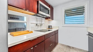 A kitchen with wooden cabinets, a microwave, a toaster, and a window with blinds. - Summer Deal Oceanfront Kona Vacation Townhouse with Lanai and Sunsets (Kailua Kona)