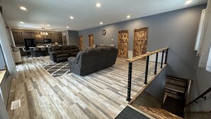 A modern living room with a gray sectional sofa, a dining area with a kitchen in the background, and a staircase with a wooden railing. - Big Chip - 2 is in the heart of the Chippewa Flowage 20 minutes from Hayward, WI (Hayward)