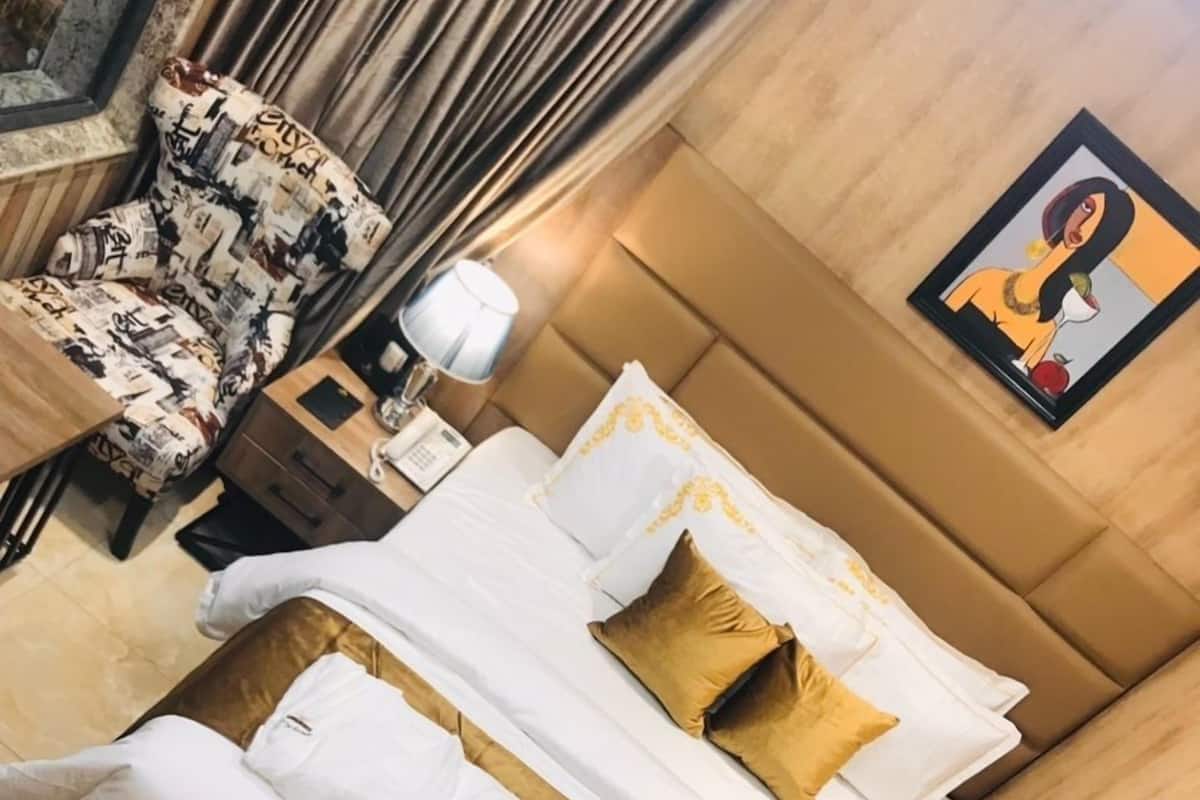 A hotel room with a bed, a sofa, a chair, a bedside table, a lamp, and a painting on the wall.