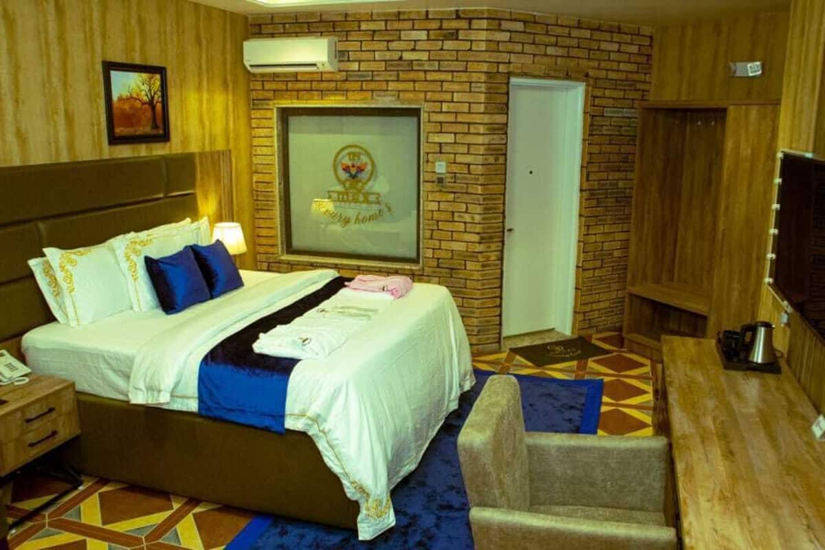 A hotel room with a bed, bedside table, lamp, and a framed picture on the wall.