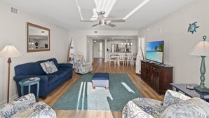 A modern living room with a blue sofa, a patterned armchair, a wooden cabinet, and a television.