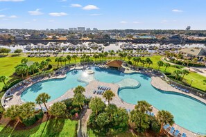 A large, curved swimming pool surrounded by palm trees and lounge chairs, with a marina and cityscape in the background.