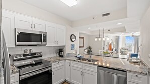 A modern kitchen with white cabinets, stainless steel appliances, and a marble countertop.