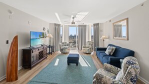 A modern living room with a large TV, a surfboard, and a view of the city.