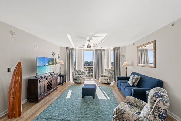 A modern living room with a large TV, a surfboard, and a view of the city.
