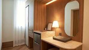 Habitación de hotel con pared de paneles de madera, lavamanos integrado, espejo, lámpara y refrigerador.