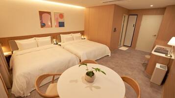 Quarto de hotel com duas camas, uma mesinha com uma planta, uma escrivaninha com abajur e uma porta.