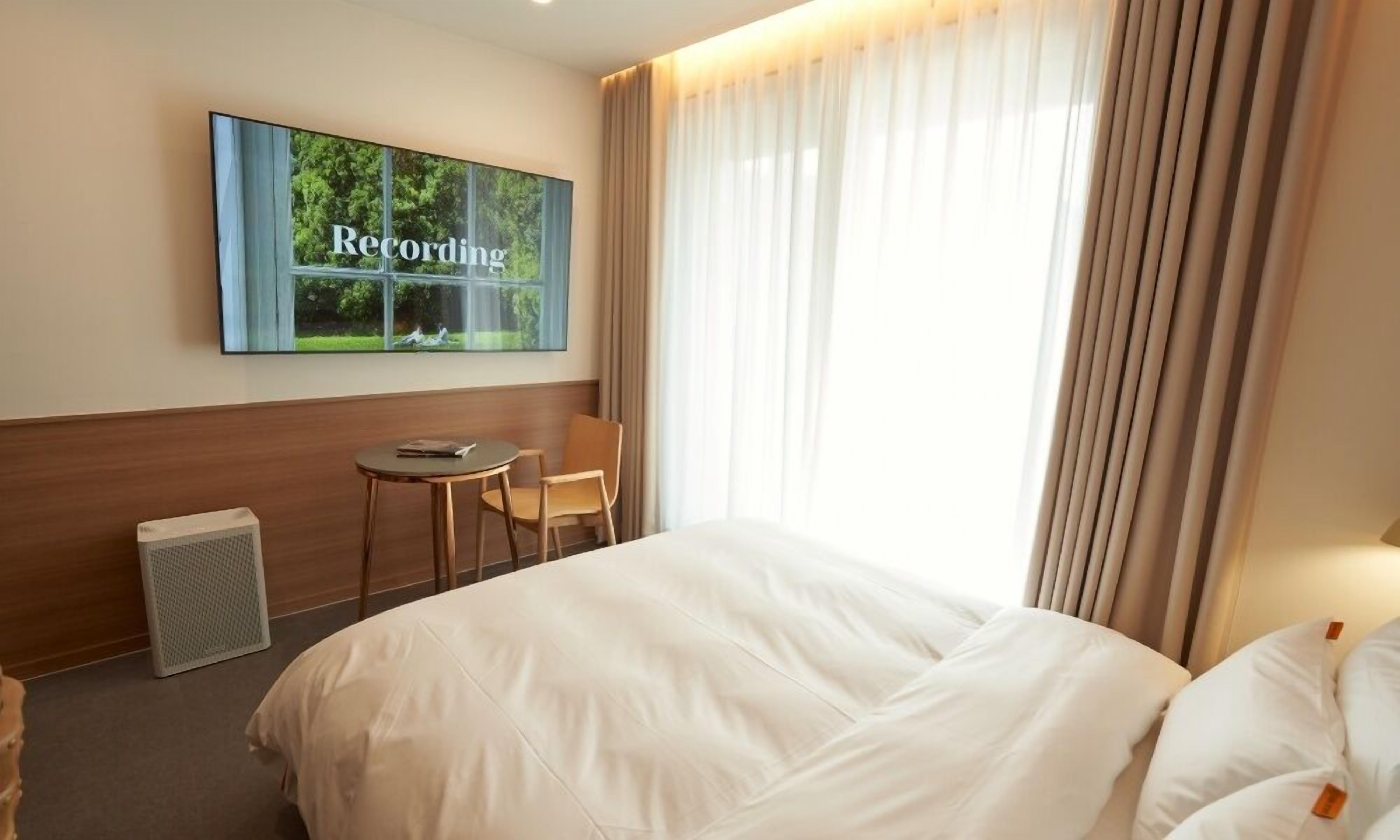 Habitación de hotel con cama, una silla, una mesita, calefactor y ventana con cortinas.
