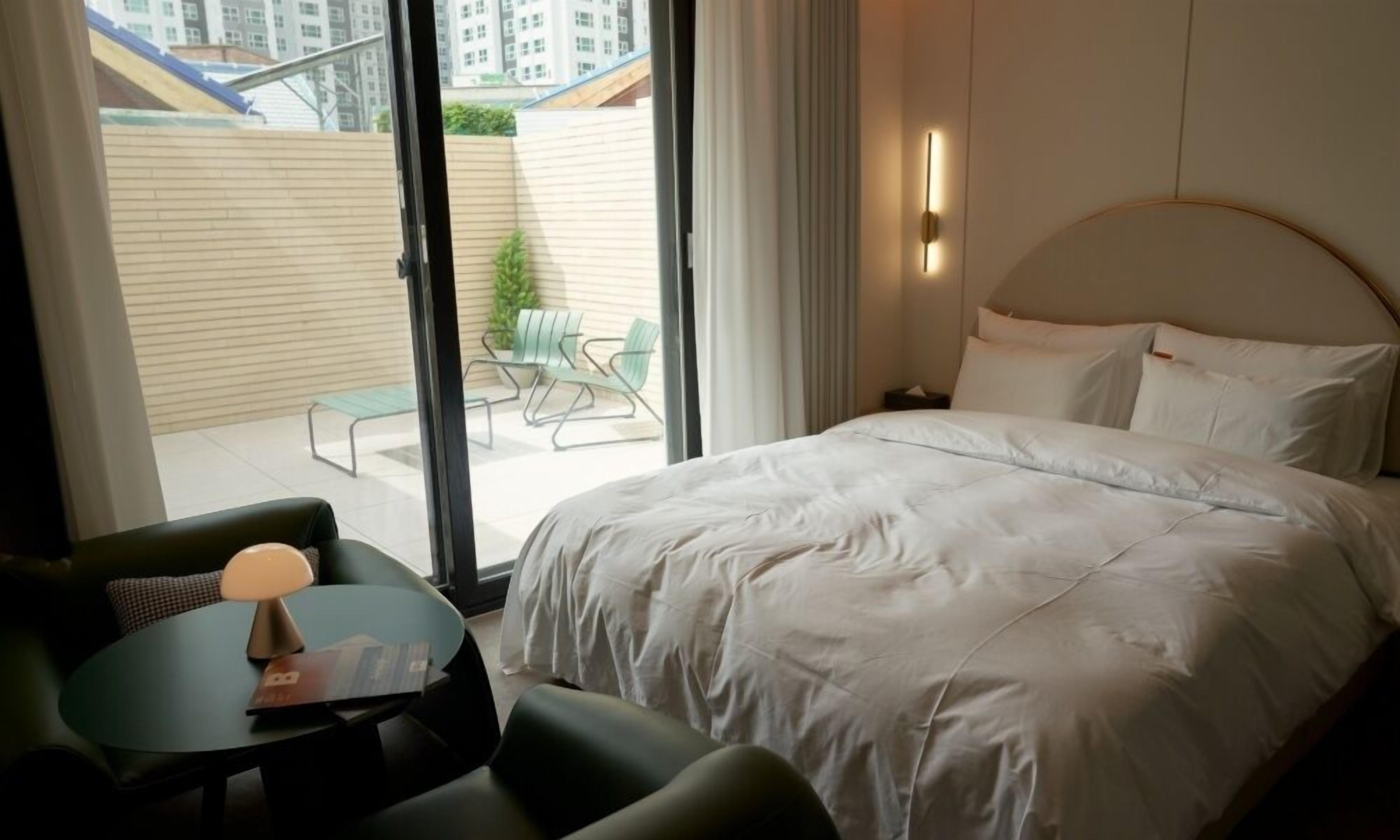 A hotel room with a large bed, a small table with a lamp, and a view of the outside balcony.