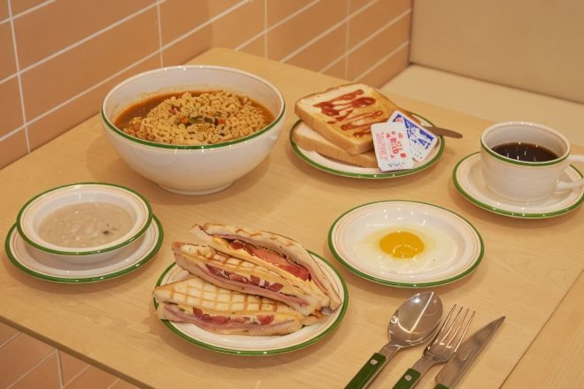 Una mesa de desayuno con un tazón de cereal, sándwiches, un plato con un huevo y una taza de café.