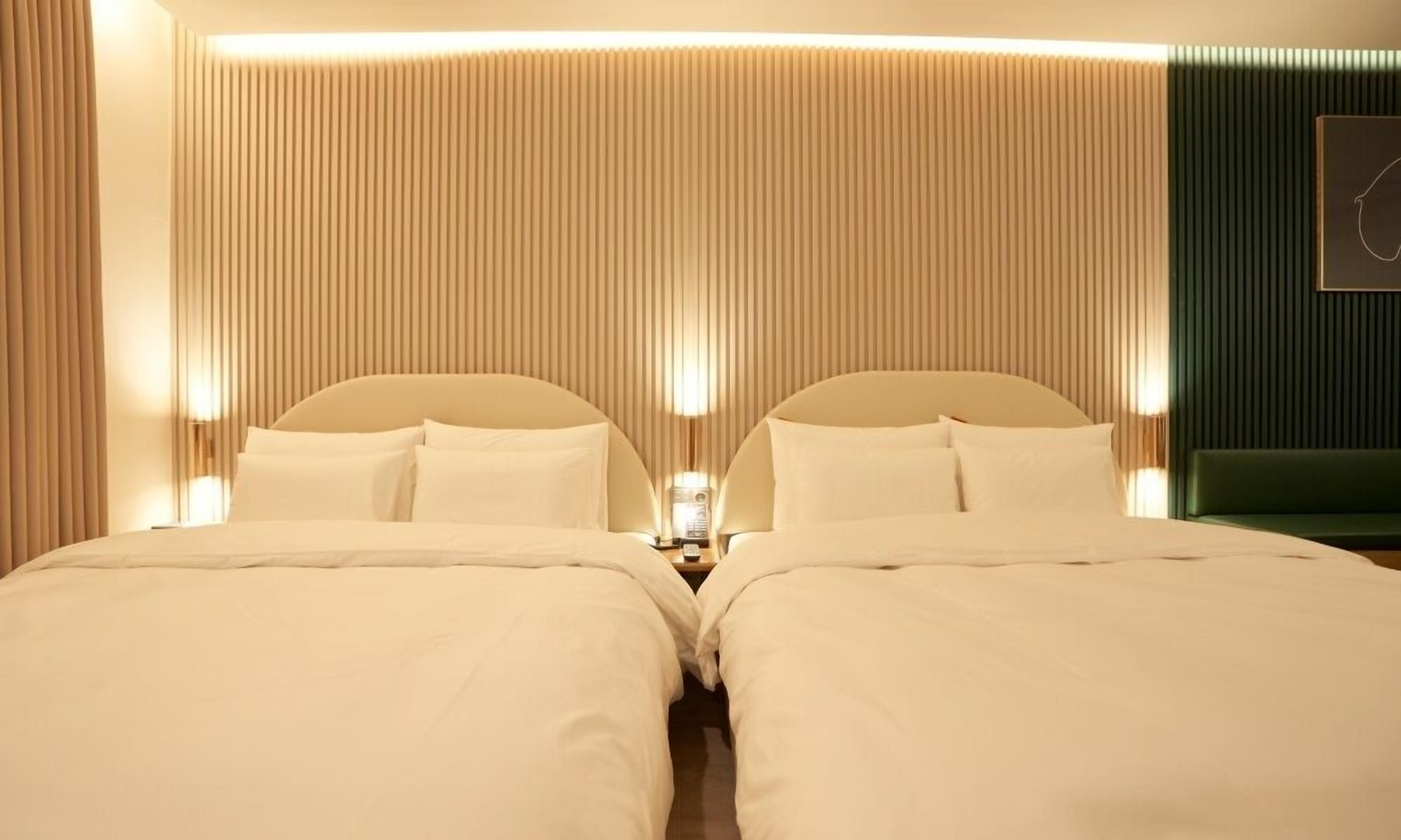 Habitación de hotel con dos camas, una mesita de noche, una lámpara de pared y una pared de acento verde.