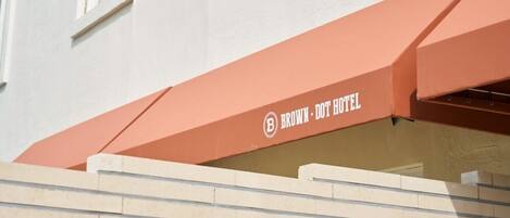 La entrada de un hotel con un cartel que dice 'BROWN DOT HOTEL' y una escalera color beige que sube hacia ella.
