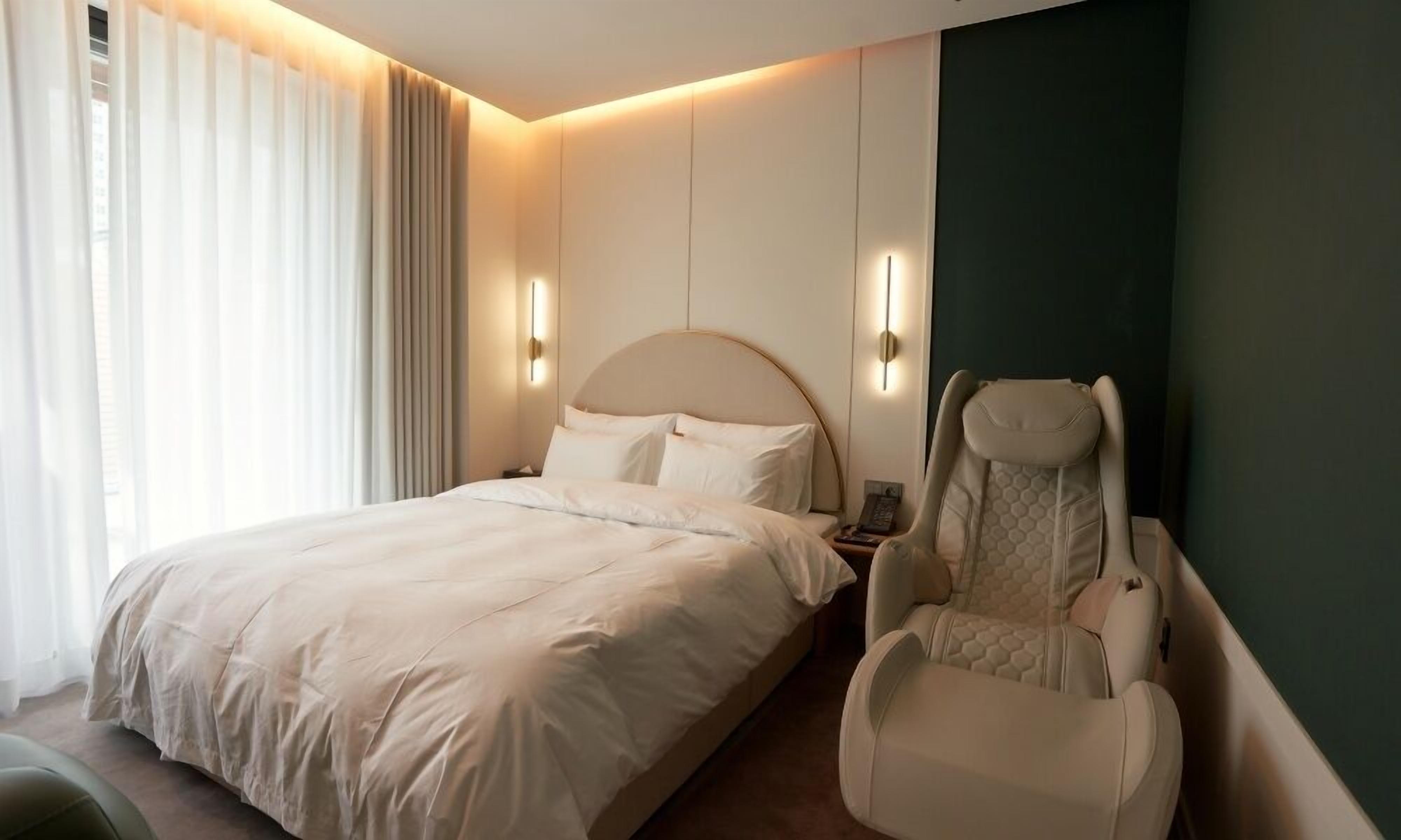 A hotel room with a bed, a massage chair, and a wall-mounted phone.