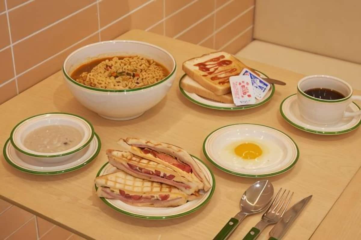 Een ontbijttafel met een kom cornflakes, boterhammen, een bord met een ei en een kop koffie.