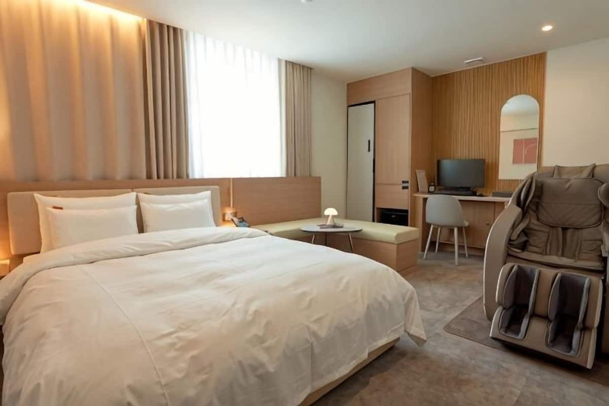 Een hotelkamer met een groot bed, een bureau met stoel, een massagestoel en een televisie.