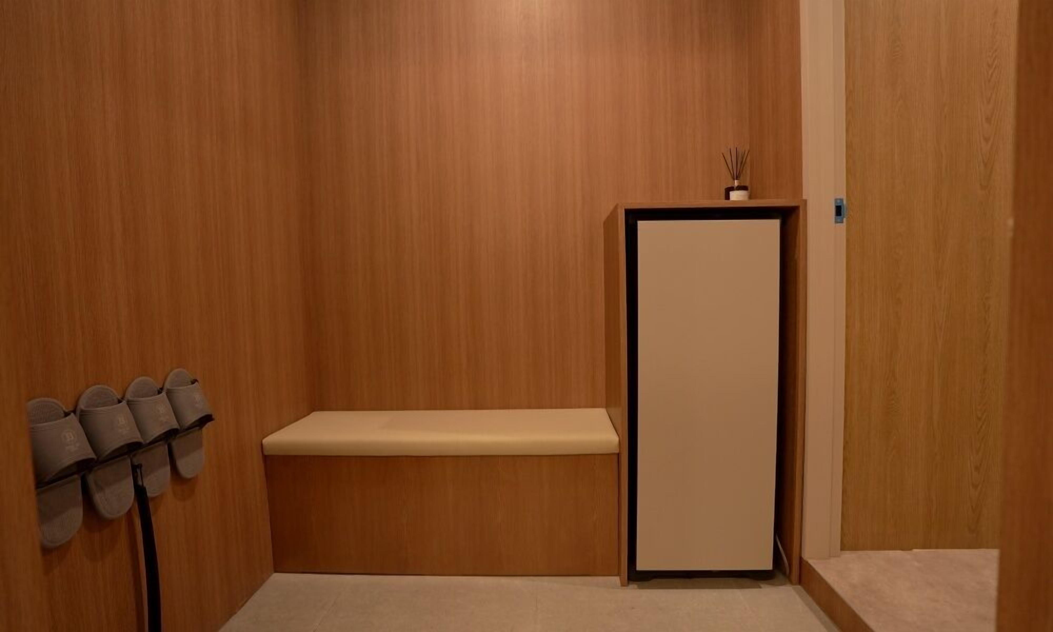 A room with a wooden wall, a bench, and a shoe rack.
