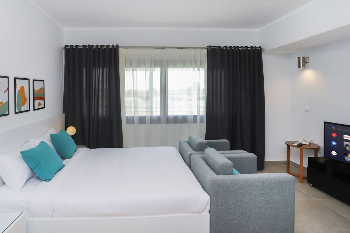 A modern hotel room with a large bed, grey sofa, and a TV.
