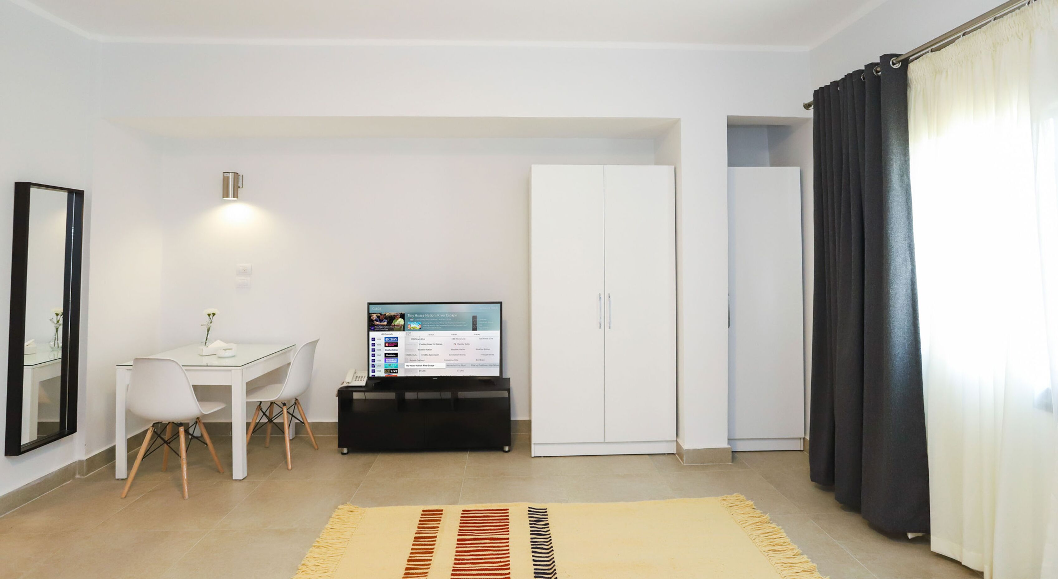 Habitación moderna y bien iluminada con un escritorio, una silla y un televisor mostrando un sitio web de bienes raíces.