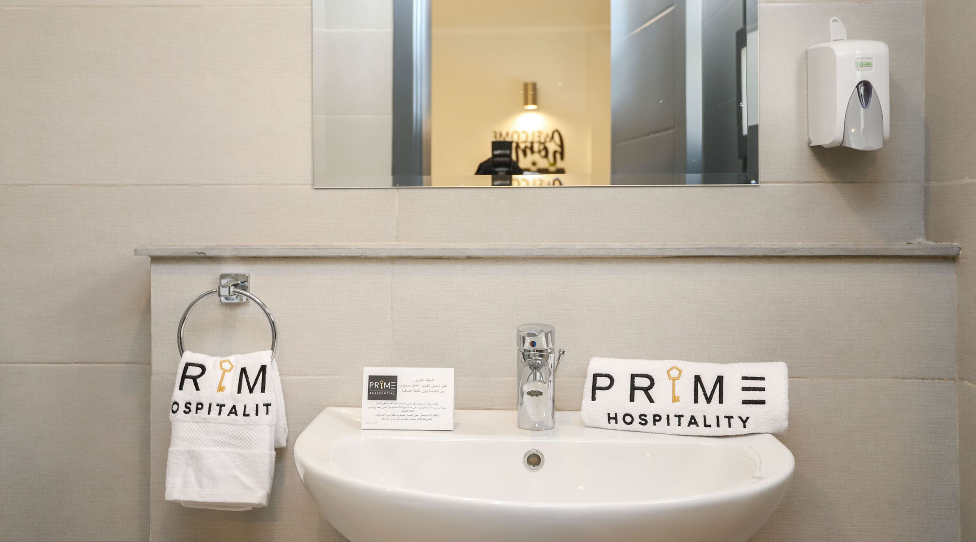 Une salle de bain avec un lavabo, deux serviettes étiquetées « RIM » et « PRIME », une bouteille en verre et une petite carte d’information.