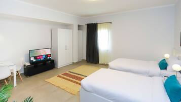 Una habitación de hotel moderna con dos camas individuales, un televisor sobre un soporte, un escritorio con una silla y un armario.