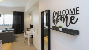 Un salon moderne avec un canapé, une table à manger et une pancarte « BIENVENUE CHEZ VOUS » accrochée au mur.