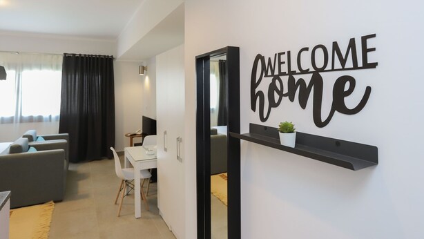 A modern living room with a sofa, a dining table, and a 'WELCOME home' sign on the wall. - Prime Inn 10th of Ramadan (Tenth of Ramadan City)