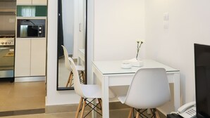 Une chambre d’hôtel moderne avec une table à manger blanche, deux chaises, un téléviseur à écran plat et un coin cuisine équipé d’un four à micro-ondes.