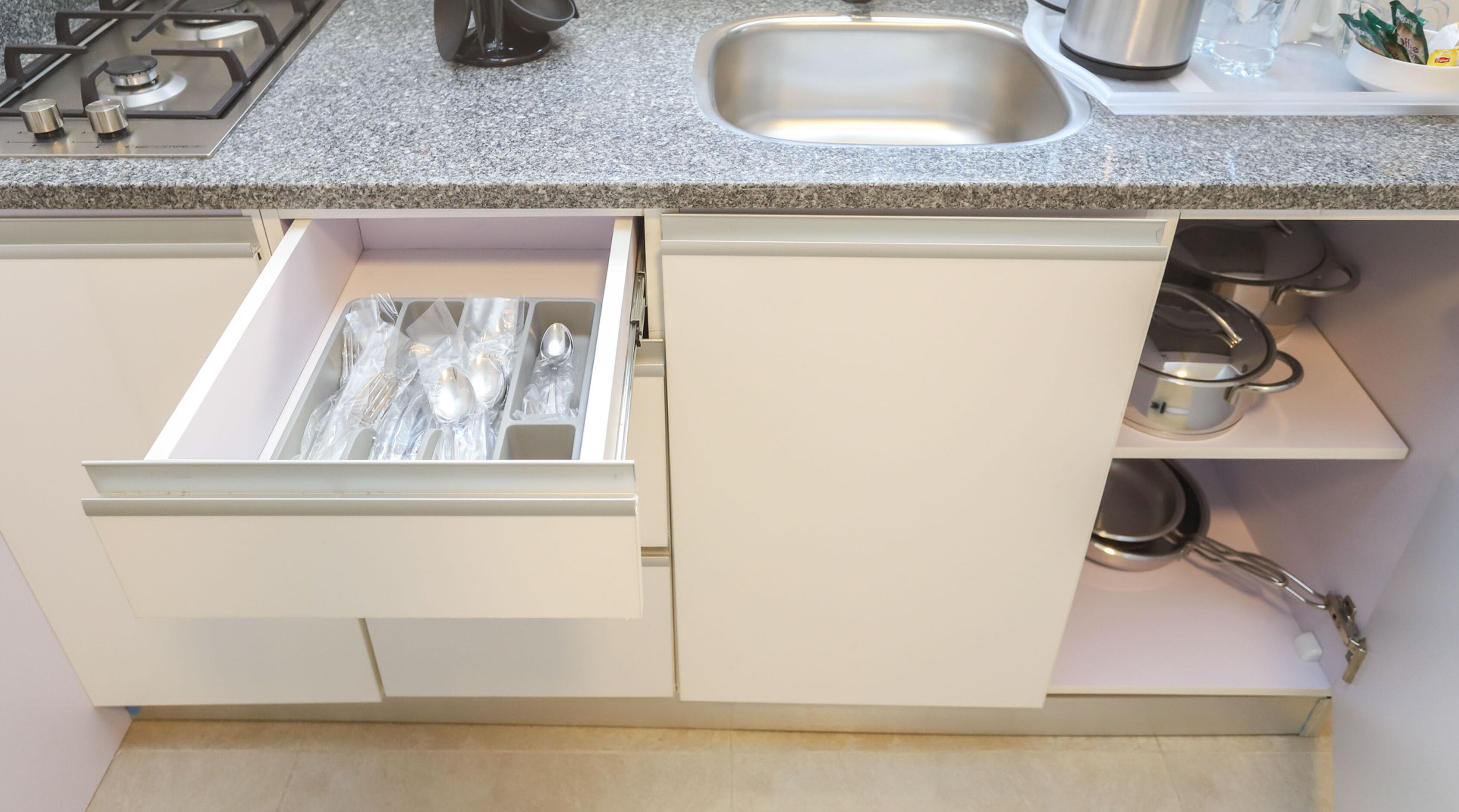 A kitchen with a granite countertop, stainless steel sink, and a drawer with utensils.